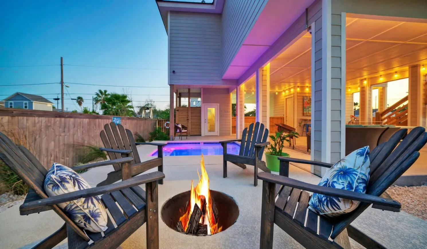 An outdoor patio with seating around a lit fire pit beside a modern house.