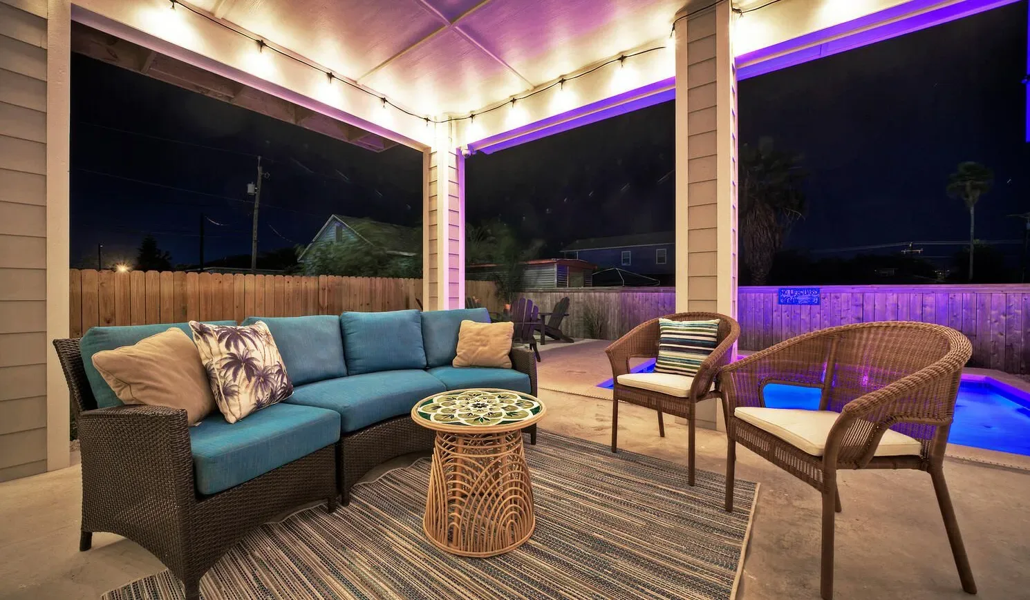 A covered outdoor seating area overlooks an illuminated pool at night.