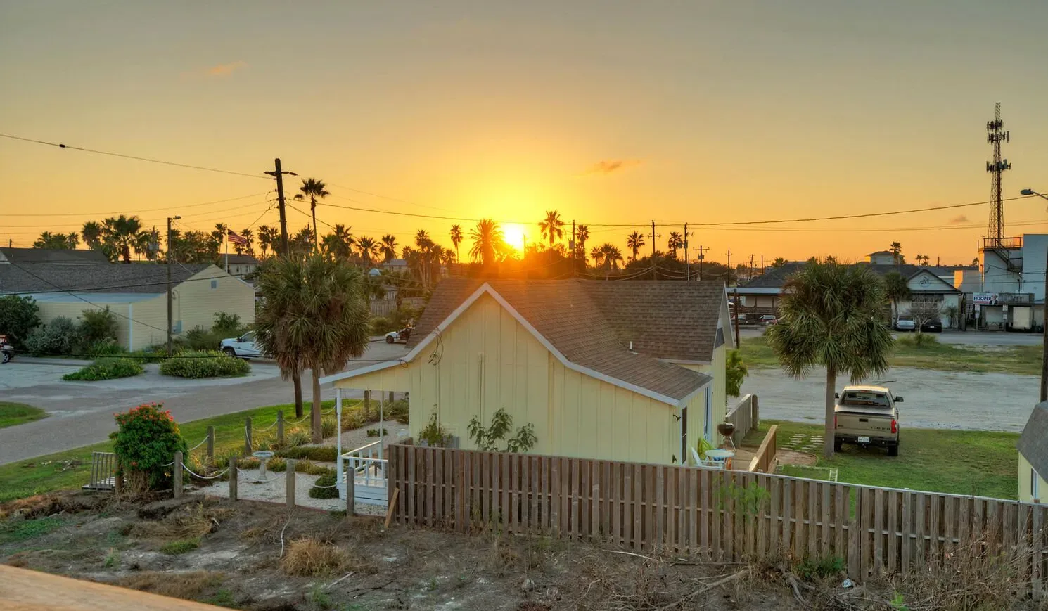 A residential neighborhood at sunset, with a wooden fence in the foreground.