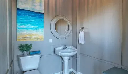 A bathroom with a pedestal sink, round mirror, and beach artwork.
