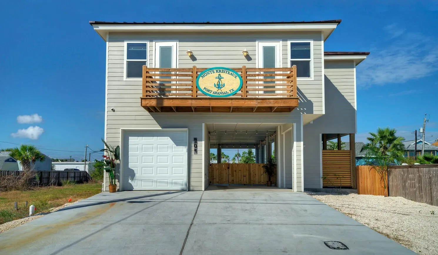 A raised coastal-style house with a wooden balcony above its driveway.