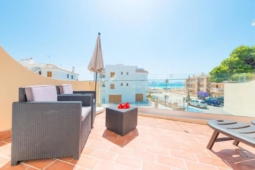 Una terraza soleada con asientos al aire libre y vistas a edificios cercanos y al mar.
