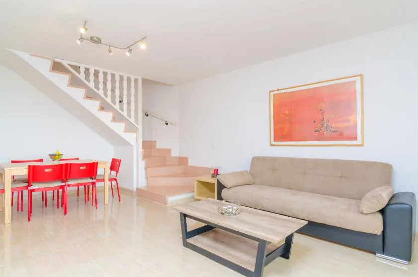 Una sala luminosa con un sofá beige, una mesa de centro y una escalera.