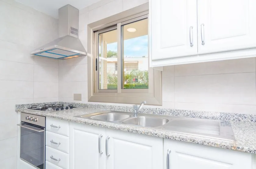 Una cocina luminosa con gabinetes blancos, una encimera y una ventana sobre el fregadero.