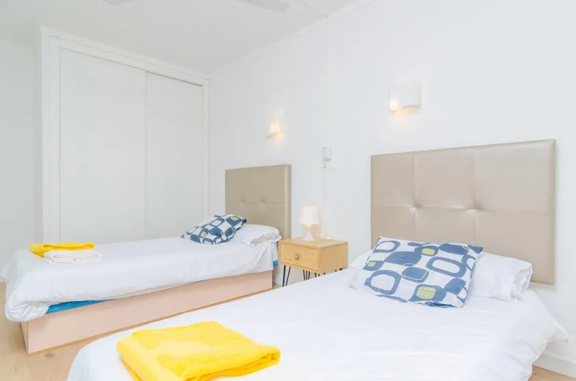 Un dormitorio luminoso con dos camas y una mesita de noche.