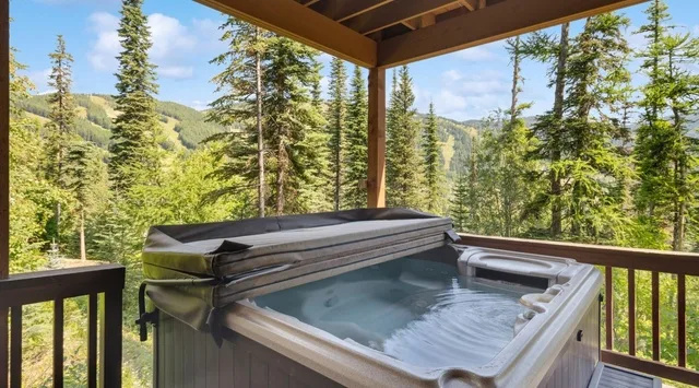 Una bañera de hidromasaje al aire libre está en una terraza cubierta con vistas a un paisaje montañoso y boscoso.