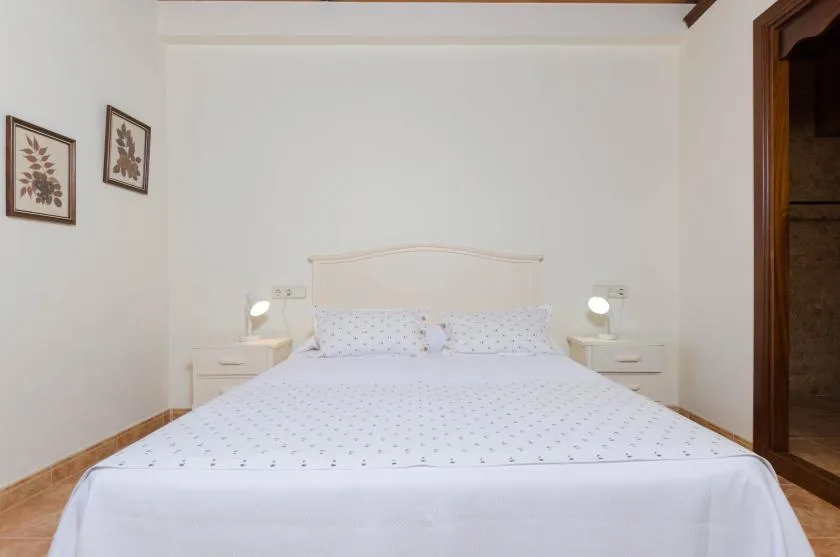 Un dormitorio con una cama, mesitas de noche y láminas florales enmarcadas.