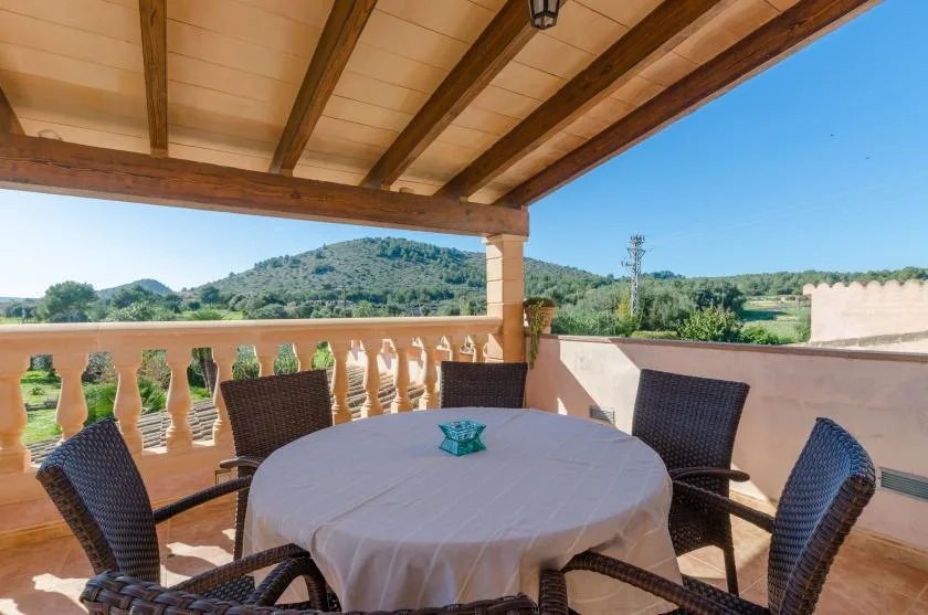 Una zona de comedor en una terraza cubierta, con mesa redonda y asientos de mimbre, da a colinas verdes.