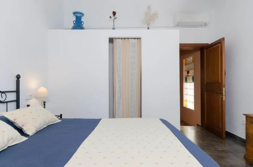 Dormitorio con una cama, una abertura estrecha con cortina y una puerta de madera abierta.