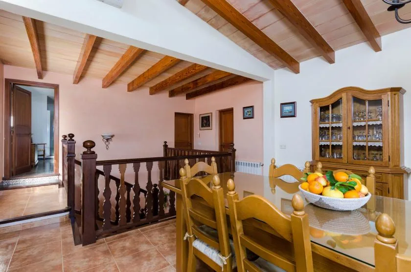 Comedor con asientos de madera y un aparador con puertas de vidrio bajo vigas expuestas.
