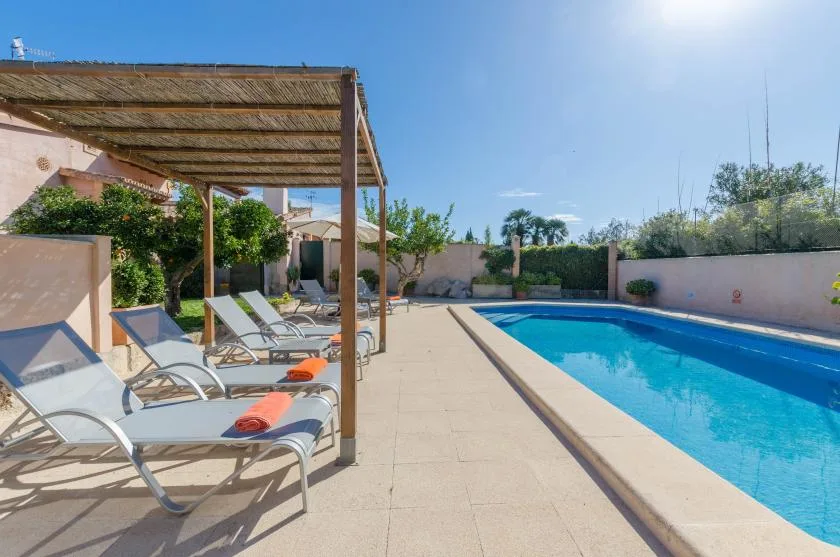 An outdoor swimming pool beside lounge seating under a shaded pergola.