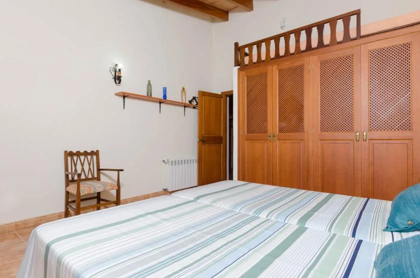 Un dormitorio con una cama a rayas, un armario de madera y una silla.