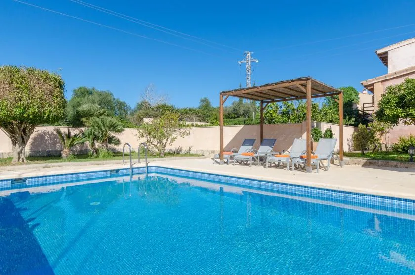Una piscina al aire libre junto a una zona de estar sombreada y un jardín.