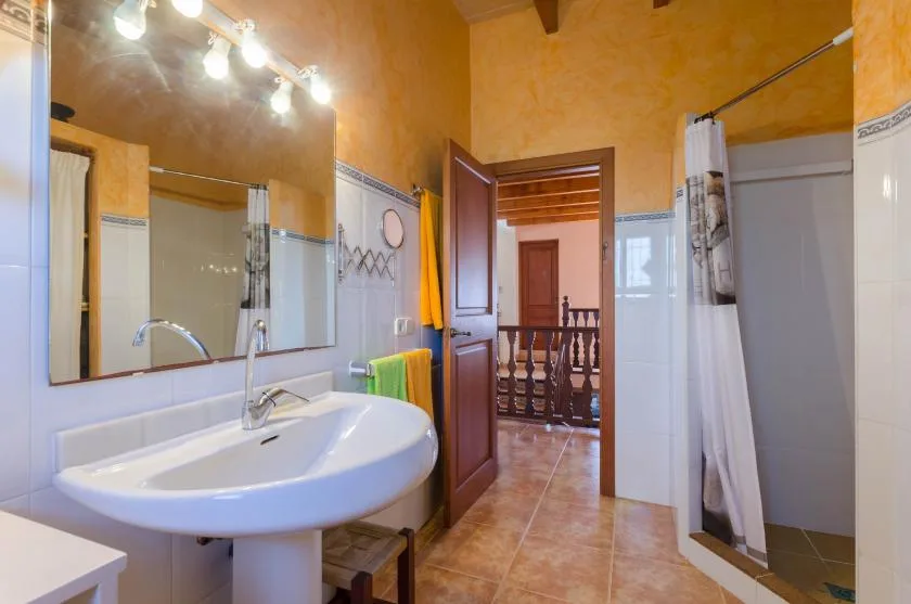 Un baño con lavabo, espejo grande y cortina de ducha junto a una puerta abierta.