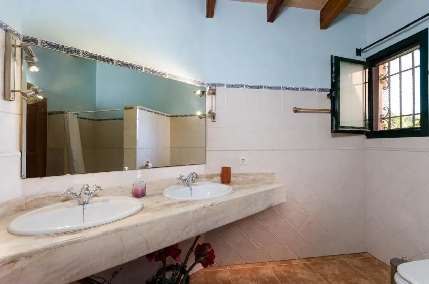 Un baño con una encimera larga, dos lavabos y una ventana abierta.