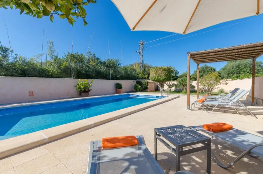 Una piscina al aire libre junto a un patio sombreado con asientos para descansar.