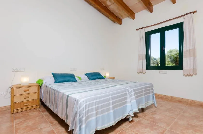 Un dormitorio con una cama, una mesita de noche y una ventana bajo vigas de madera.