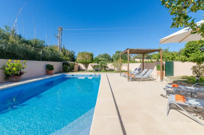 Una piscina al aire libre junto a un patio pavimentado con tumbonas y una pérgola.