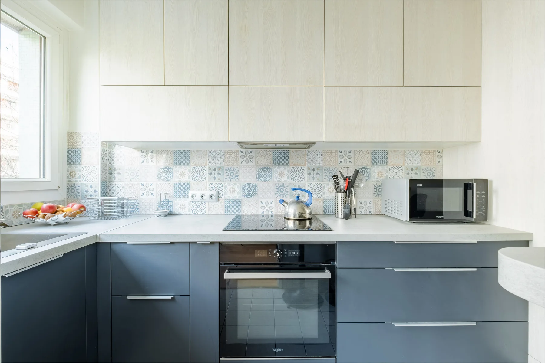 A modern kitchen with dark lower cabinets, a patterned backsplash, and countertop appliances.