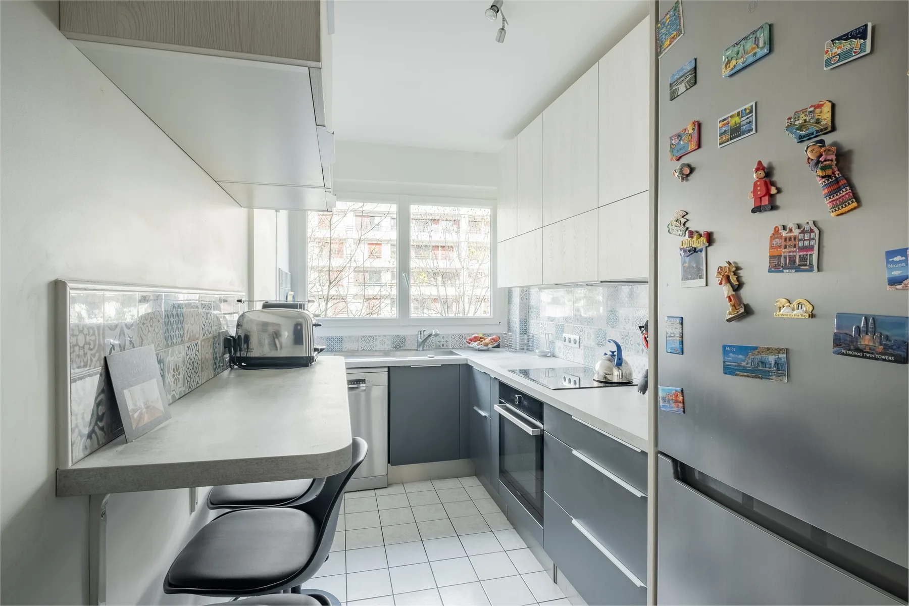 A bright modern kitchen with pale countertops, dark lower cabinets, and a refrigerator.