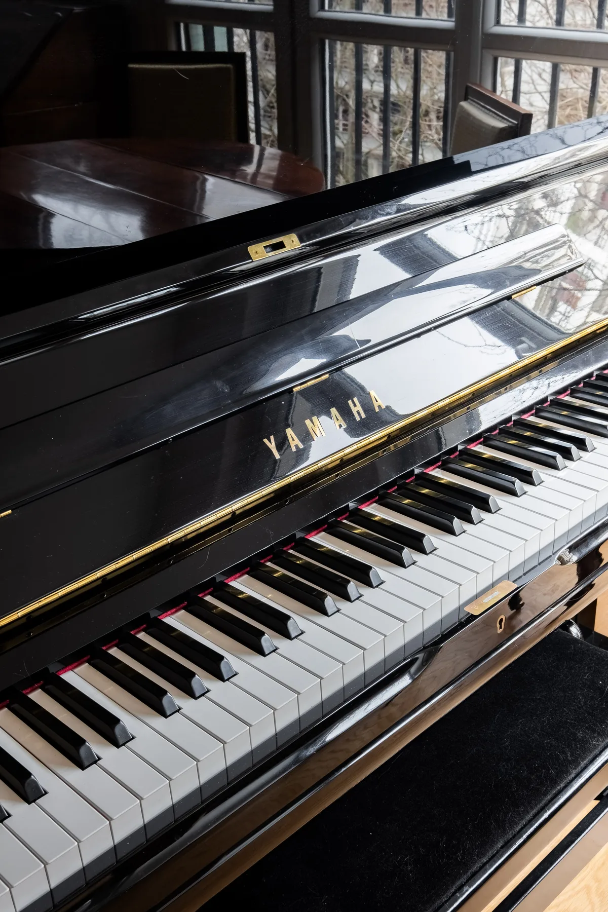 A glossy black grand piano with its keyboard open beside large windows.