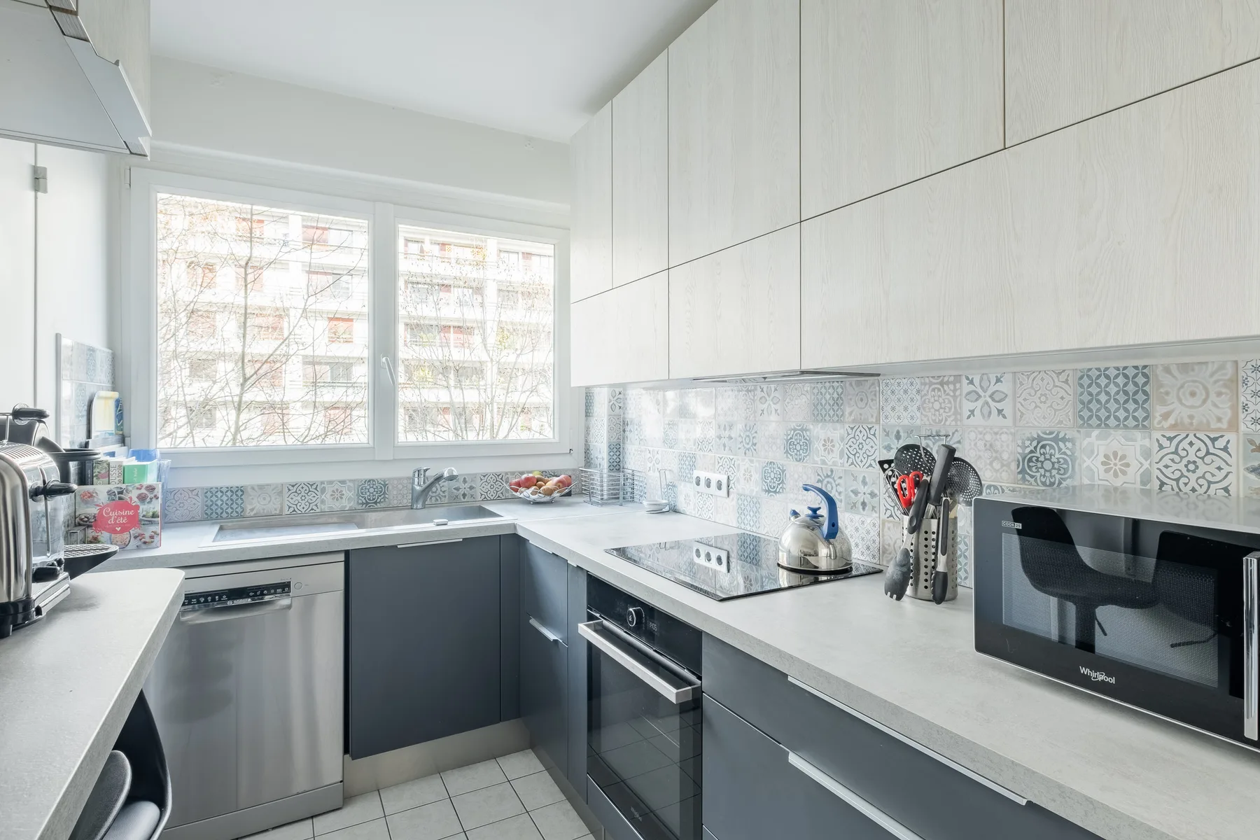 A modern kitchen with pale cabinets, gray countertops, and a window above the sink.