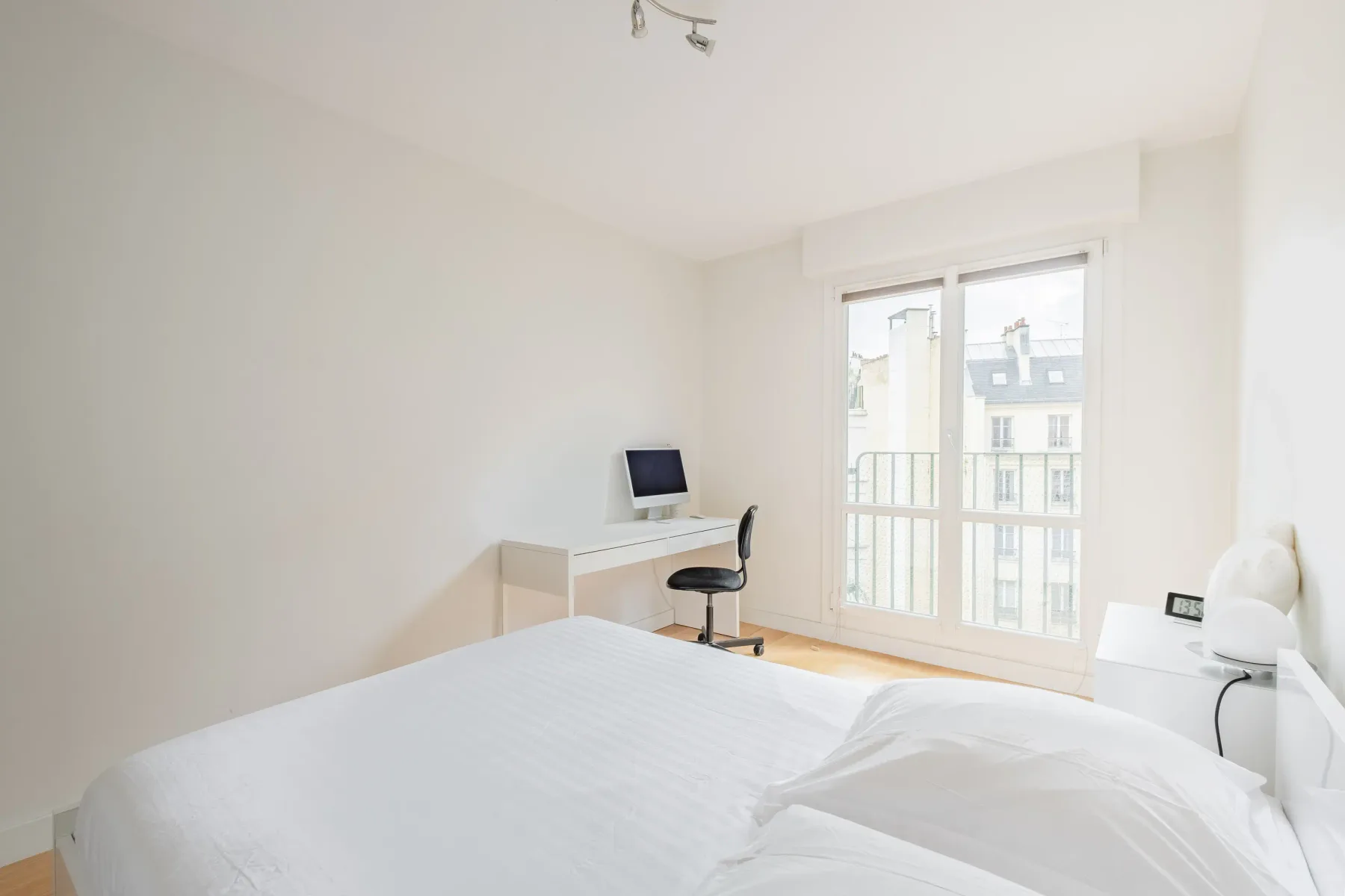 A bright bedroom with a bed, desk, and large windows.