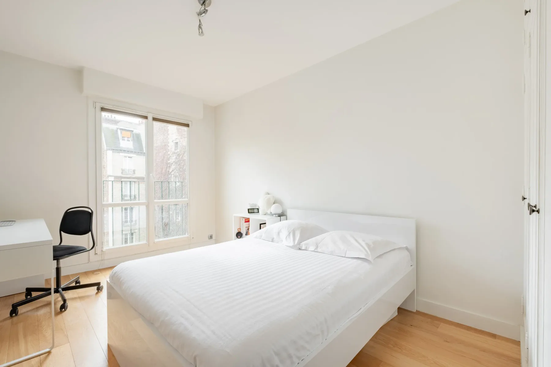 A bright bedroom with a white bed and large windows.