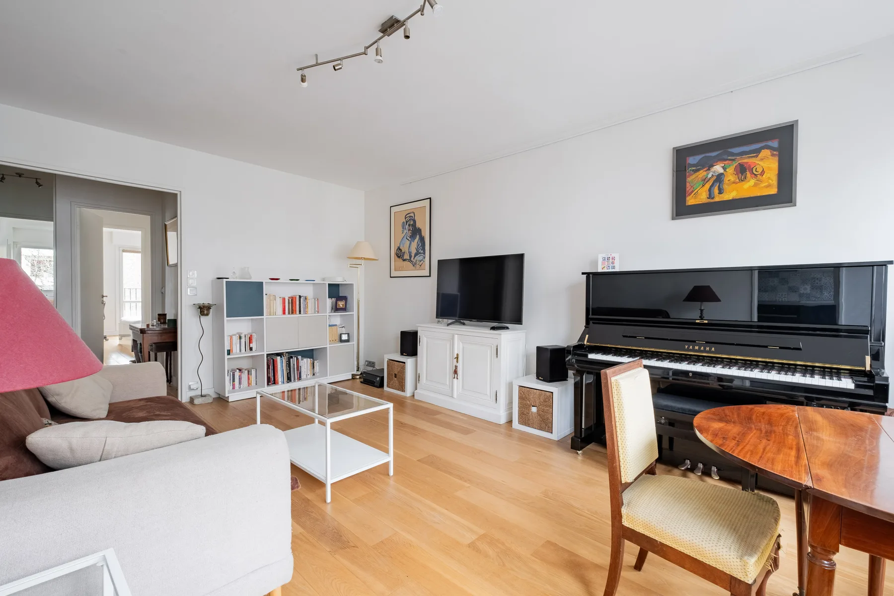 A bright living room with seating, a television, bookshelves, and a piano.