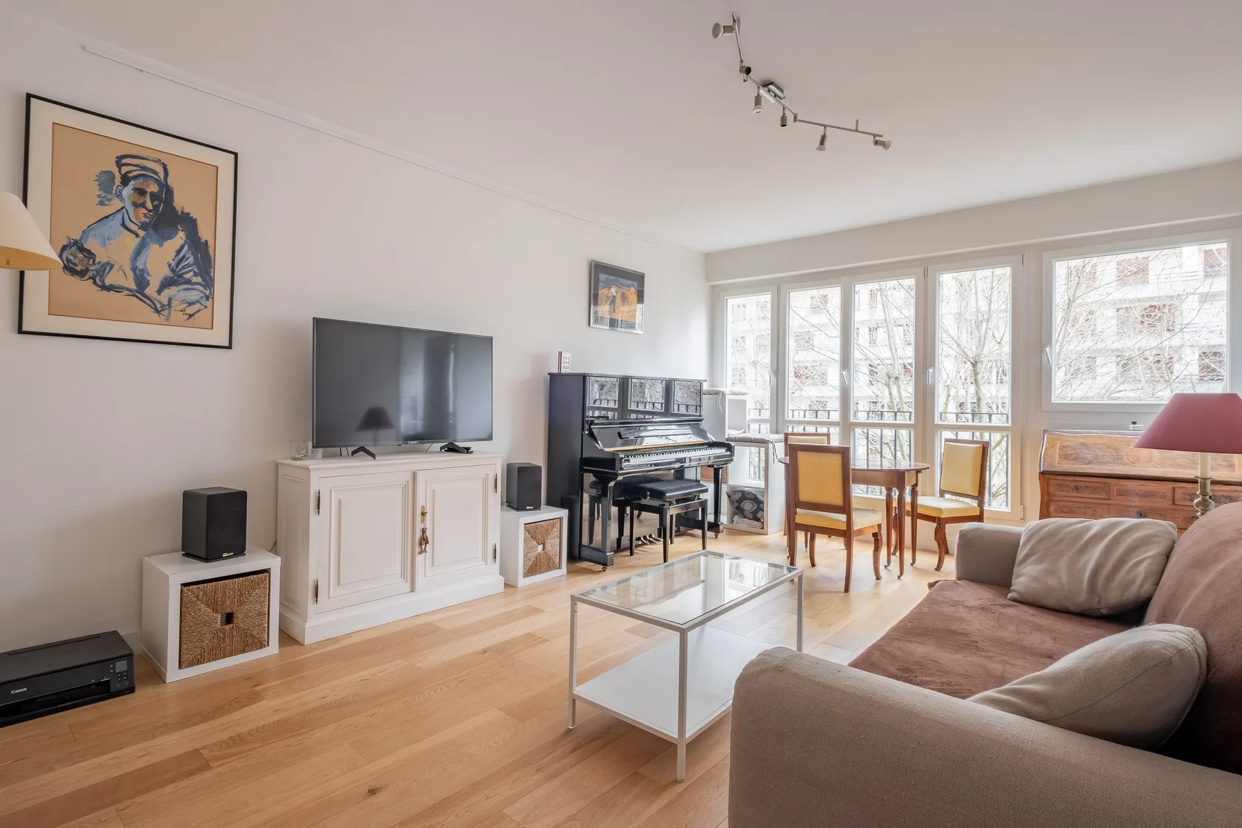 A bright living room with a seating area, television, and dining table by large windows.