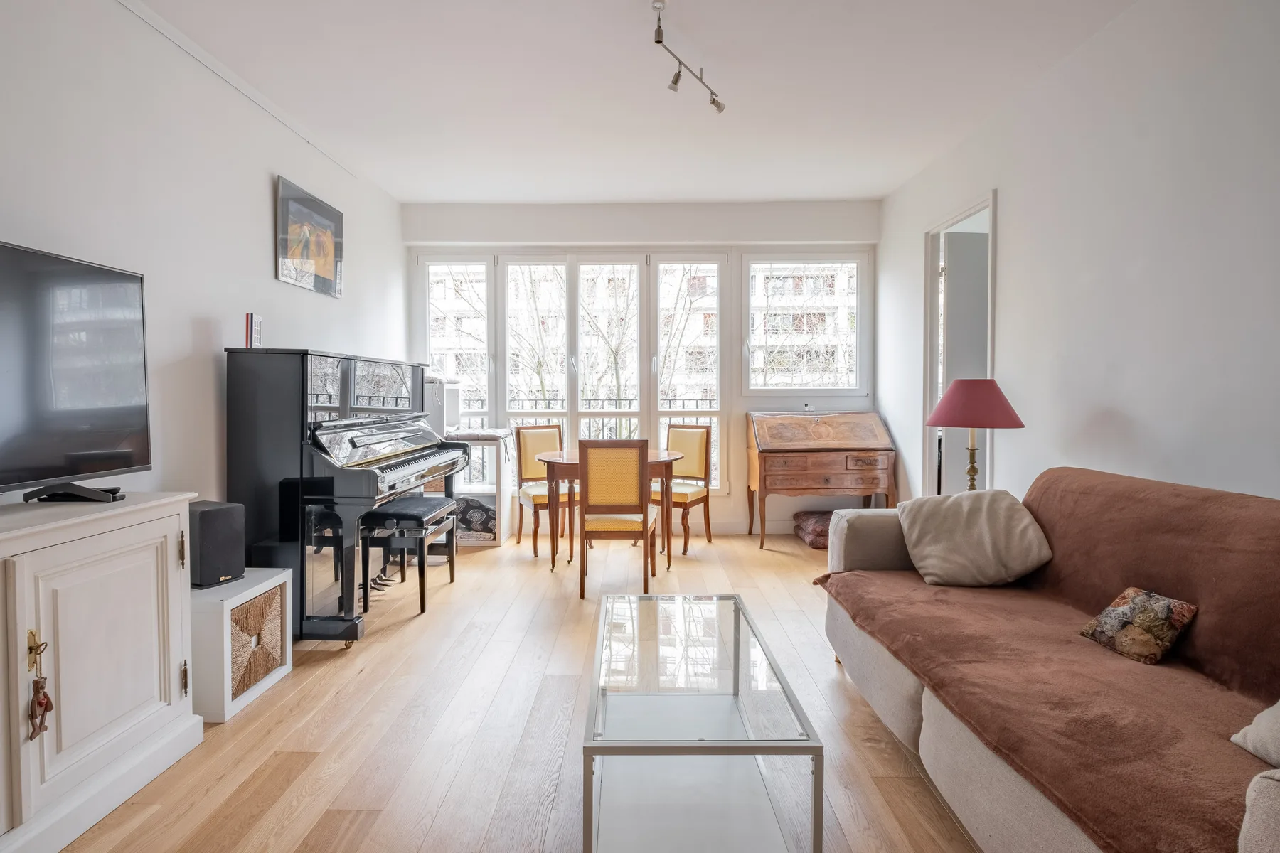 A bright living room with a piano, dining table, and seating beside large windows.