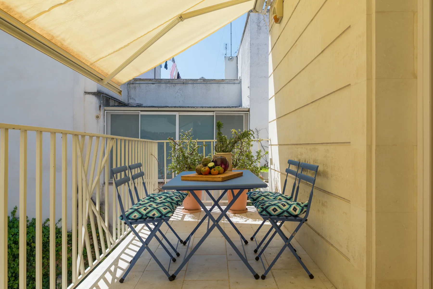 A sunny balcony dining area with a table, chairs, and a retractable awning.