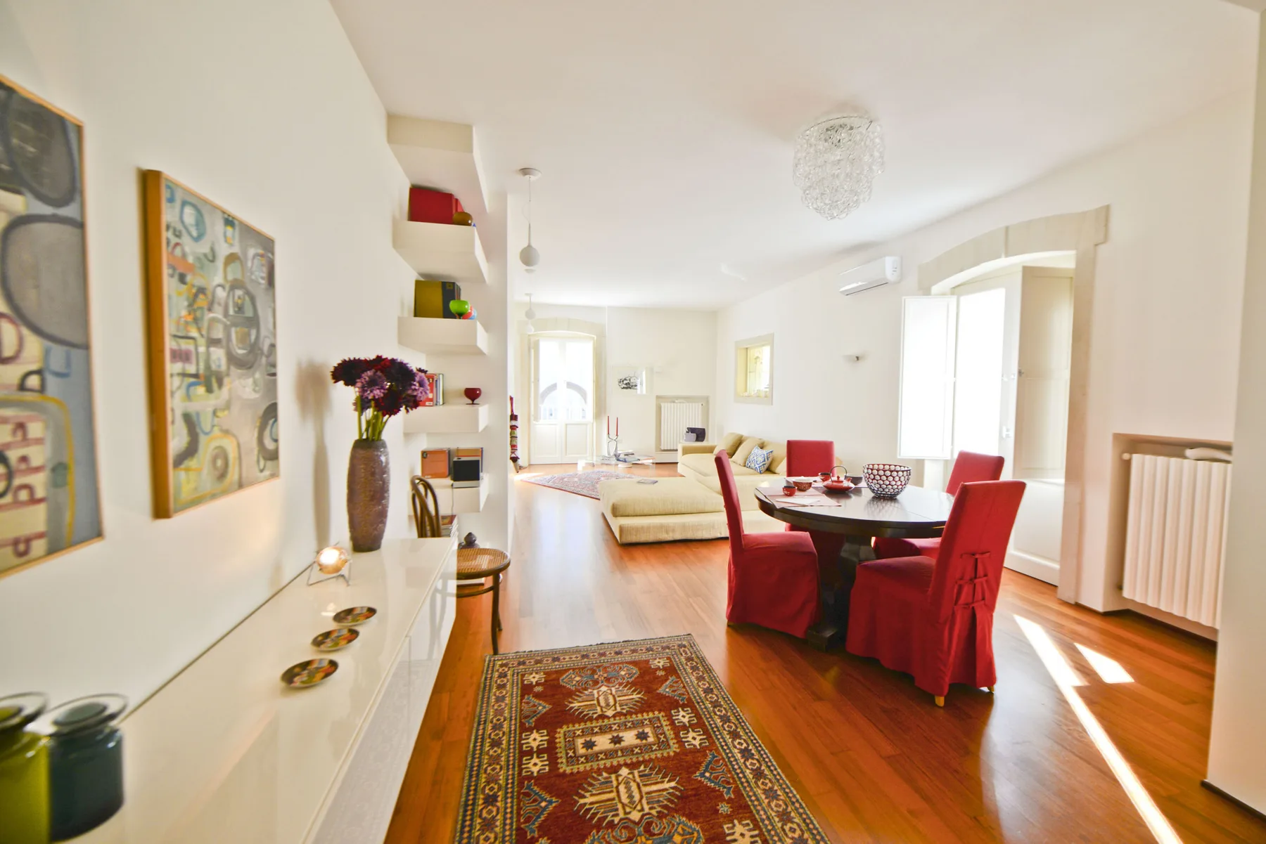 A bright living and dining room with colorful seating and framed artwork.