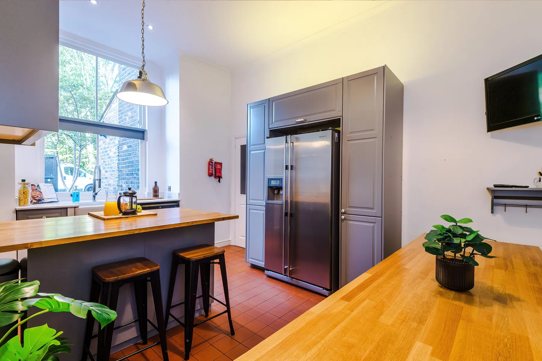 A kitchen with a stainless-steel refrigerator, wooden counters, and bar seating.
