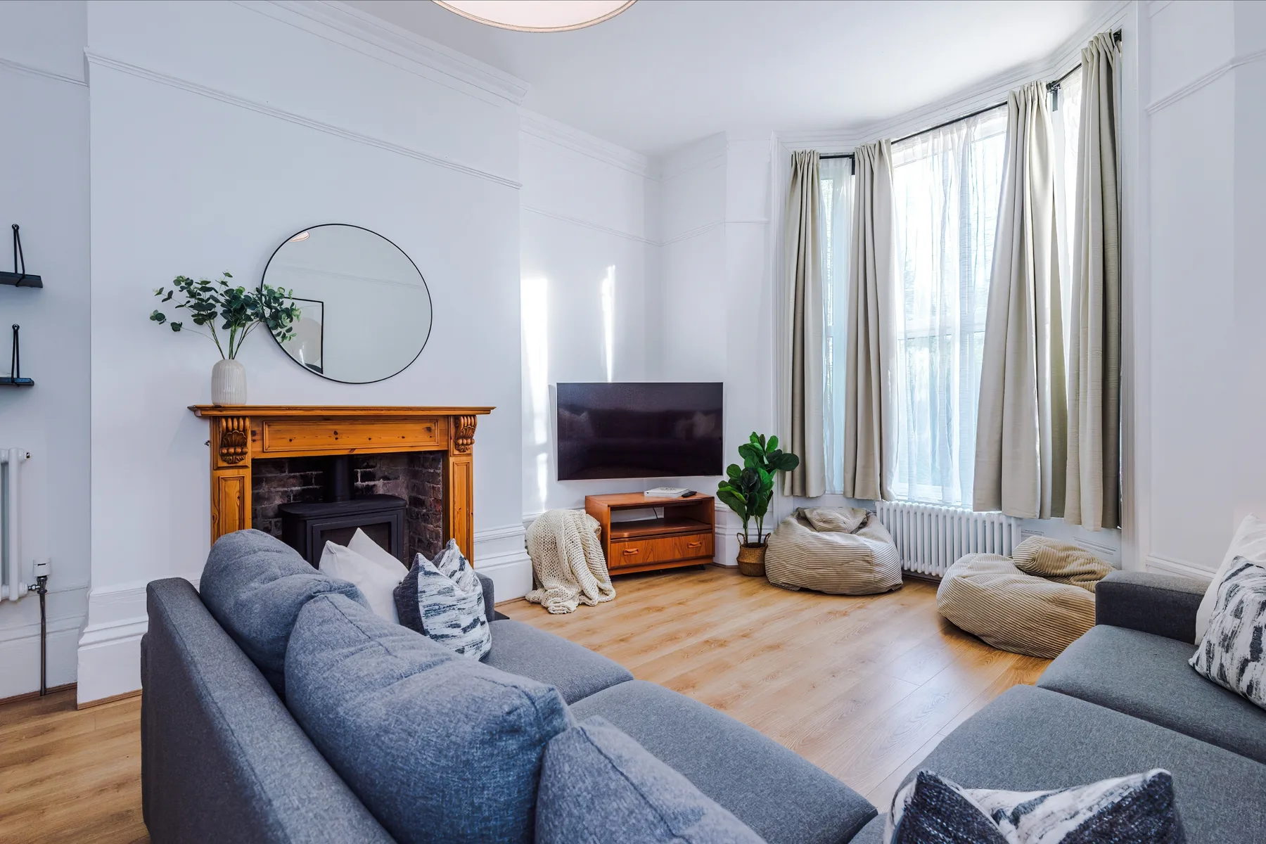A bright living room with seating, a fireplace, and tall curtained windows.