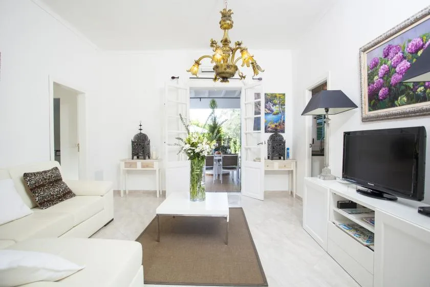 A bright living room with white seating, a television, and a glass coffee table.