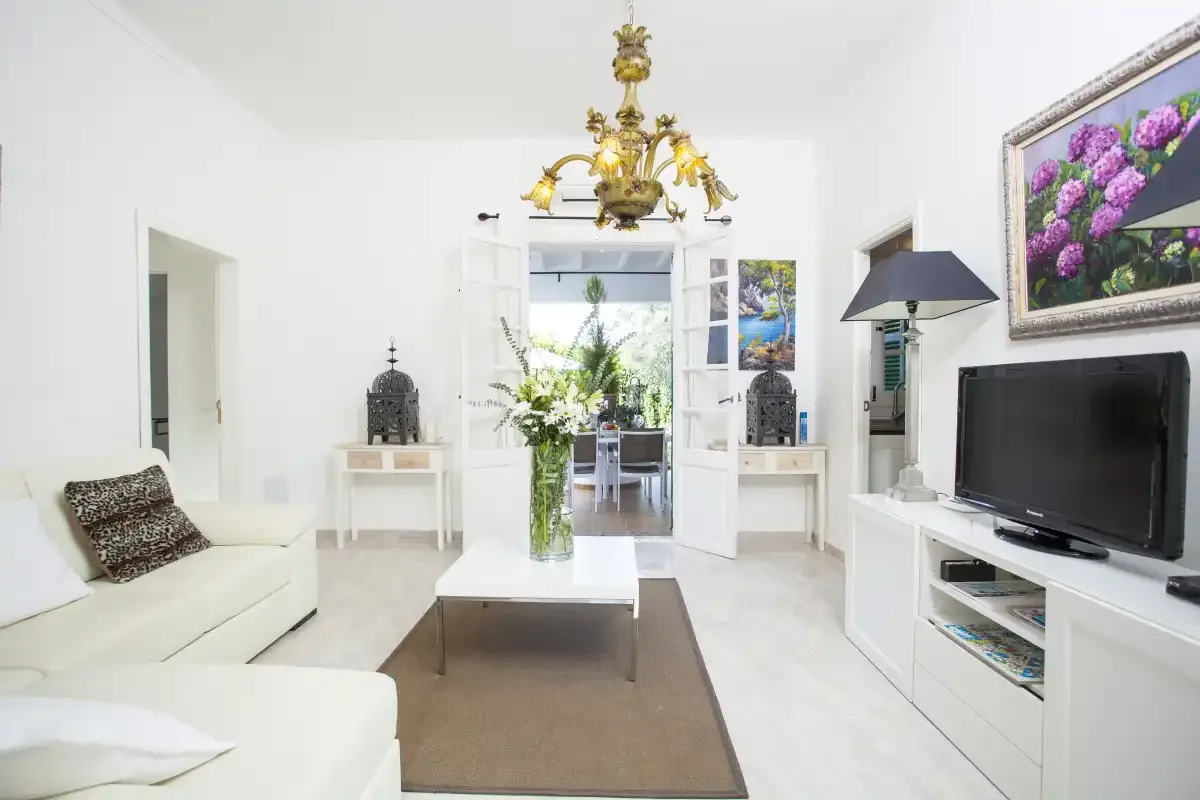 A bright living room with white seating, a television, and a coffee table.