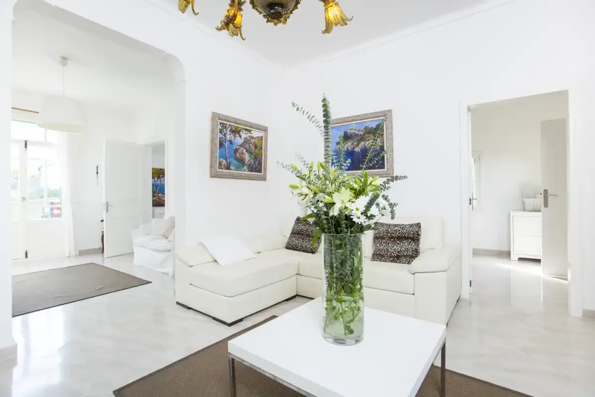 A bright living room with white seating and a glass vase of flowers.