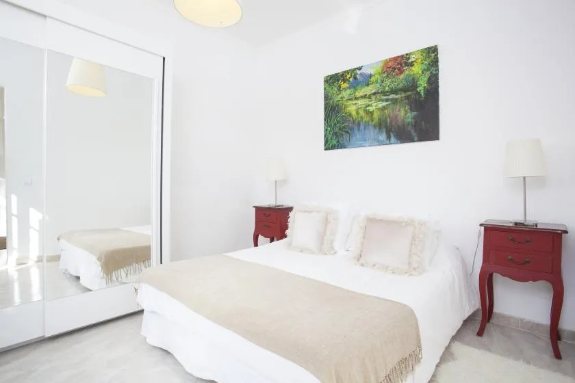 A bright bedroom with a bed, mirrored closet doors, and red bedside tables.