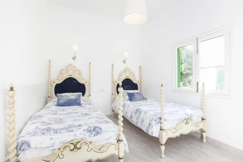 A bright white bedroom with two beds and a window.