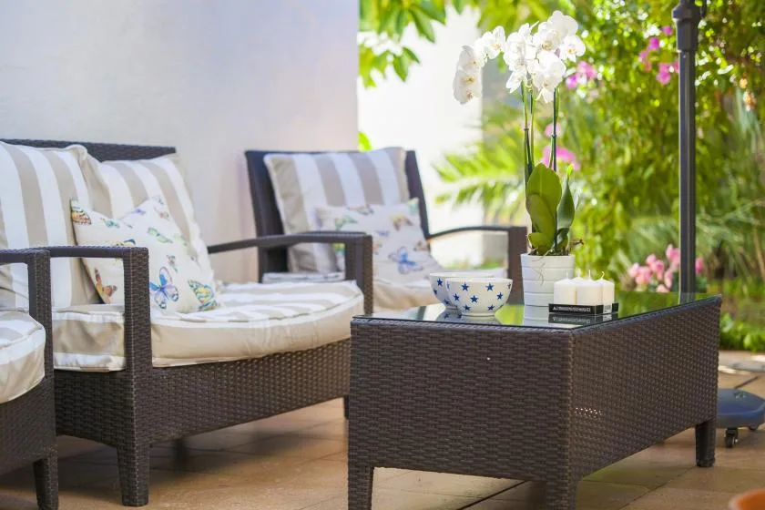 A patio seating area with cushioned chairs and a low table beside flowering plants.