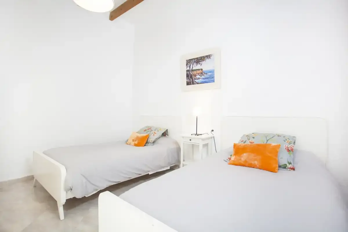 A bright bedroom with two beds and a small bedside table.