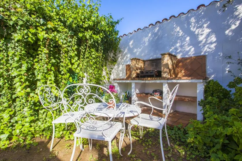 An outdoor patio with white metal seating beside a built-in barbecue.