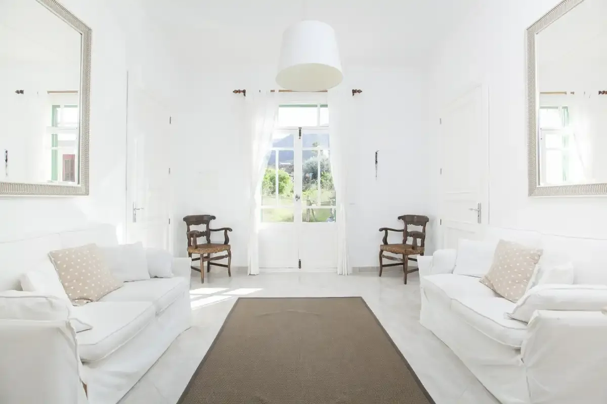 A bright living room with white seating and a window overlooking greenery.