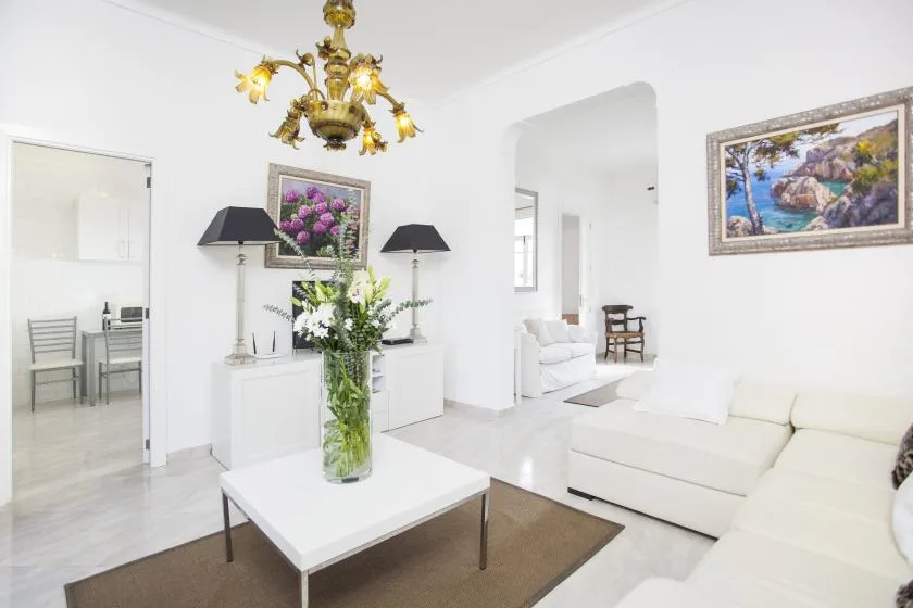 A bright living room with white seating, a coffee table, and floral arrangements.