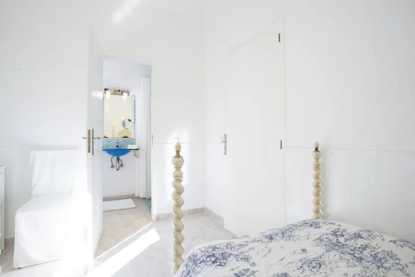 A bright bedroom with a patterned bedspread and an open doorway to a washroom.
