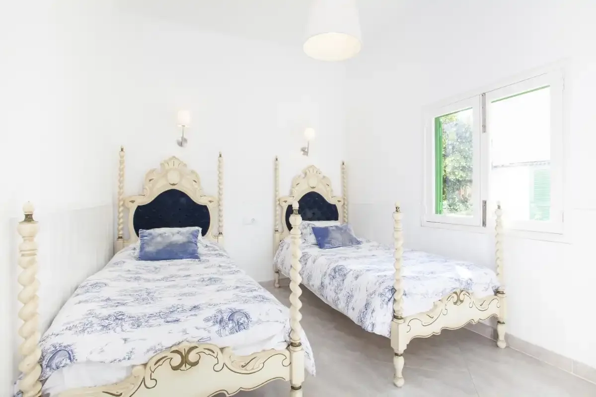 A bright bedroom with two beds and a window.