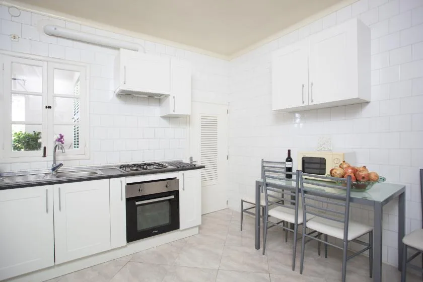 A bright kitchen with white cabinets, a cooking range, and a dining table.