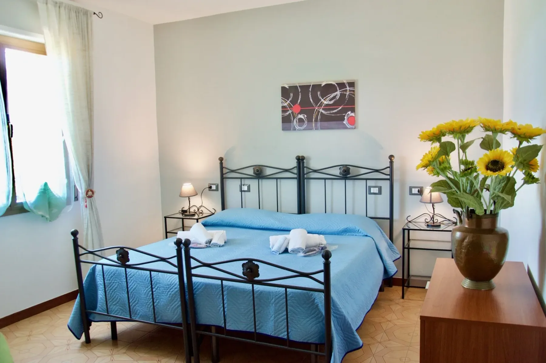Habitación de huéspedes con una cama y un jarrón de girasoles.