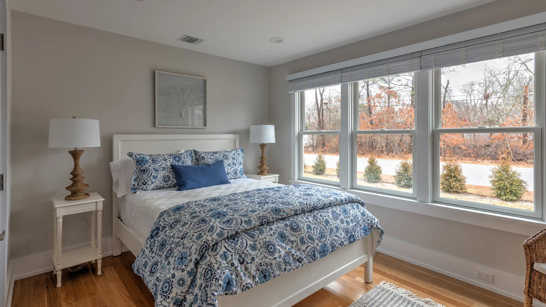 Un dormitorio con una cama cubierta de ropa de cama azul estampada junto a grandes ventanas.